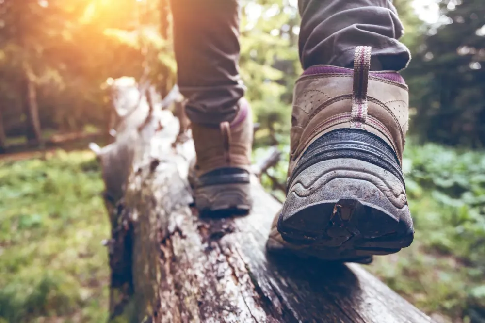 Close up of a pair of feet wearing hiking boots crossing an old log in the forest